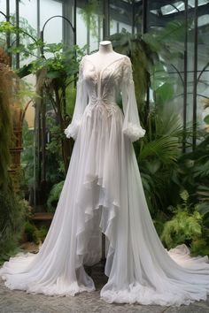 a white wedding dress is on display in a glass room with plants and greenery