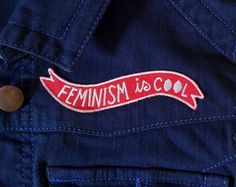 a red feminist is cool sticker on the back of a blue jean jacket,