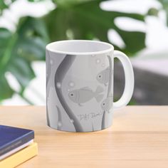 a white coffee mug sitting on top of a wooden table next to a book and plant