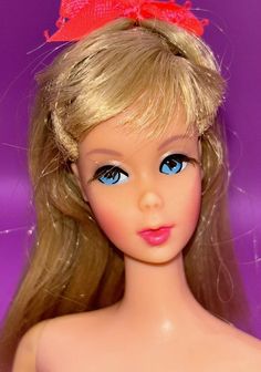 a doll with blonde hair and blue eyes wearing a red bow on top of her head