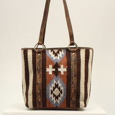 This Ariat wool blanket tote by M&F Western Products is brown with orange, blue and ivory in a southwestern pattern. Genuine leather on back, on handles and edge tooling. Zip closure on top of back to keep your items safe. Details Ariat Wool Blanket Tote Brown Measures: 15 x 13 x 4-1/2 Southwestern Pattern Genuine Leather Inside 2 Small Pockets, 1 Large Zip Pocket Zip Closure Southwestern Brown Rectangular Shoulder Bag, Southwestern Style Brown Rectangular Shoulder Bag, Brown Southwestern Rectangular Shoulder Bag, Brown Southwestern Style Shoulder Bag For Everyday Use, Southwestern Hand Tooled Bags For Everyday Use, Southwestern Patterns, Brown Tote, M F, Wool Blanket