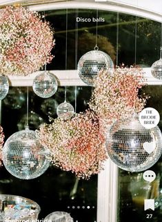 several disco balls hanging from the ceiling with pink flowers in them and some silver dishes