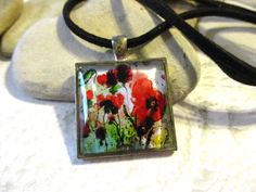 a square glass pendant with red and green flowers on it sitting on a black cord