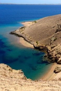 a body of water sitting on the side of a hill next to a sandy beach