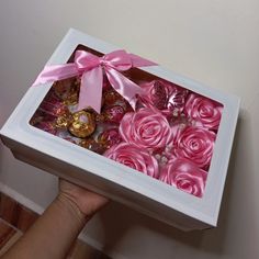 a person is holding a box with pink roses and chocolates in it that are wrapped in satin ribbon