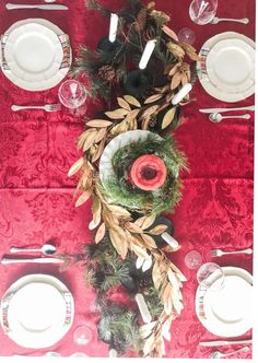 the table is set with plates, silverware and greenery for an elegant christmas centerpiece