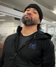 a man with a beard wearing a black hoodie and standing in an office building