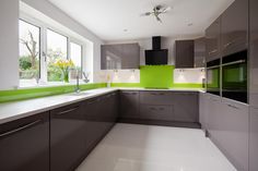 a modern kitchen with green accent wall and white counter tops, along with gray cabinets