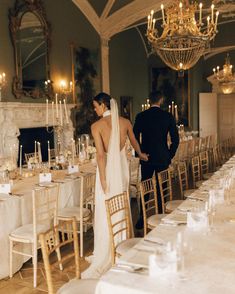 a bride and groom standing at the end of a long table with white linens