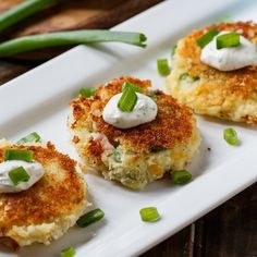 three crab cakes with sour cream and green onions on a white platter next to asparagus