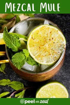 a cup filled with ice and limes on top of a table next to some mint leaves