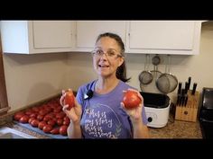 a woman is holding an apple in her hand and smiling at the camera while standing next to some tomatoes