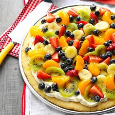 a fruit pizza is cut into slices and sits on a checkered table cloth