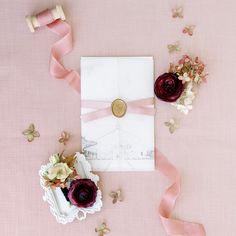 an envelope with pink ribbon and flowers on it next to some ribbons that are tied around the envelope