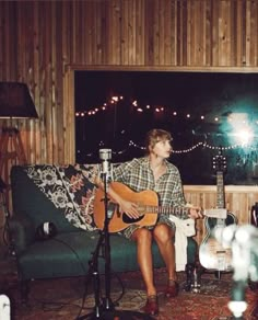 a man sitting on top of a couch holding a guitar in front of a window