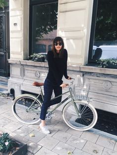 a woman standing next to a bike on the sidewalk