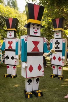 some people are dressed up like playing cards in the grass and one is wearing a top hat