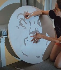 a woman sitting on the floor next to a giant paper cut out of a man's face