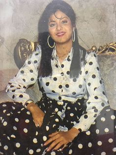 a woman sitting on top of a chair wearing polka dot pants and large hoop earrings