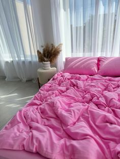 a bed with pink sheets and pillows next to a window