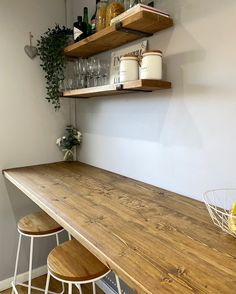 a kitchen counter with two wooden stools next to it and shelves on the wall