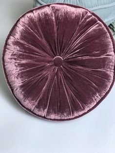 a purple velvet round pillow sitting on top of a white table next to a blue cushion