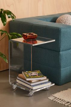 a glass table with books on it in front of a couch and potted plant