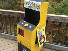 a yellow arcade game machine sitting on top of a wooden deck next to a fence