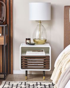 a nightstand with a lamp on top of it next to a bed