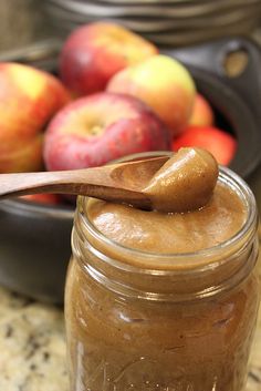 a jar filled with peanut butter next to a bowl of apples and a wooden spoon