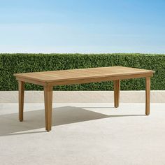 a wooden table sitting on top of a cement floor next to a hedge covered wall