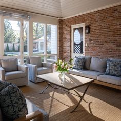 a living room filled with furniture and windows next to a brick wall in front of a door