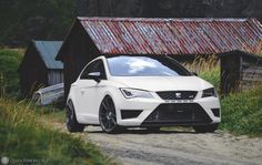 a white car is parked in front of a barn and some grass on a dirt road