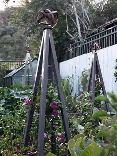 two metal sculptures in the middle of a garden with purple flowers and greenery around them