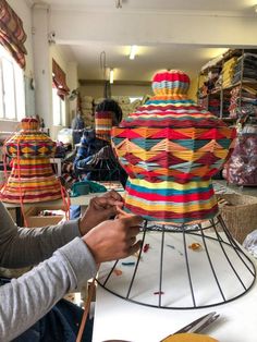 a woman sitting at a table working on a colorful object with scissors and yarn in front of her