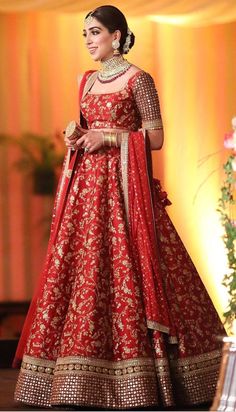 a woman in a red and gold bridal gown standing on a stage with her hands behind her back