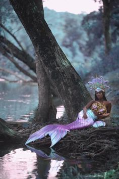 a mermaid sitting on the ground next to a tree