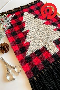 a red and black blanket with a white christmas tree on it next to some scissors