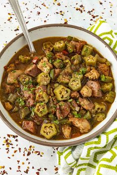 a bowl filled with meat and vegetables on top of a green towel next to a spoon