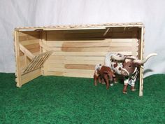 a toy cow and calf stand in front of a wooden crate with grass on the floor