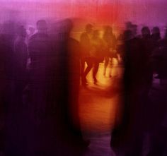 blurry photograph of people standing in front of a red and purple wall with an orange light