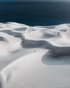 a person standing on top of a snow covered slope next to the ocean in winter