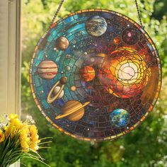 a stained glass sun catcher hanging on a window sill with flowers in front of it