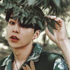 a young man is holding his hair back and looking at the camera while standing in front of some trees