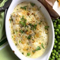 a white bowl filled with food next to green peas and bread on top of a table