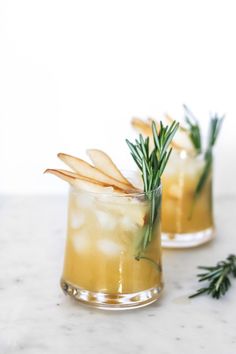 two glasses filled with lemonade and rosemary garnish on top of a marble counter