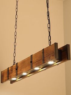 a wooden light fixture with four lights hanging from it's sides and chains on the ceiling