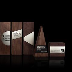 three wooden awards are displayed on a black surface with white and silver labels in the middle