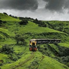 a train traveling through a lush green countryside under a cloudy sky on top of a hill