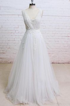 a white wedding dress on a mannequin stand in front of a brick wall